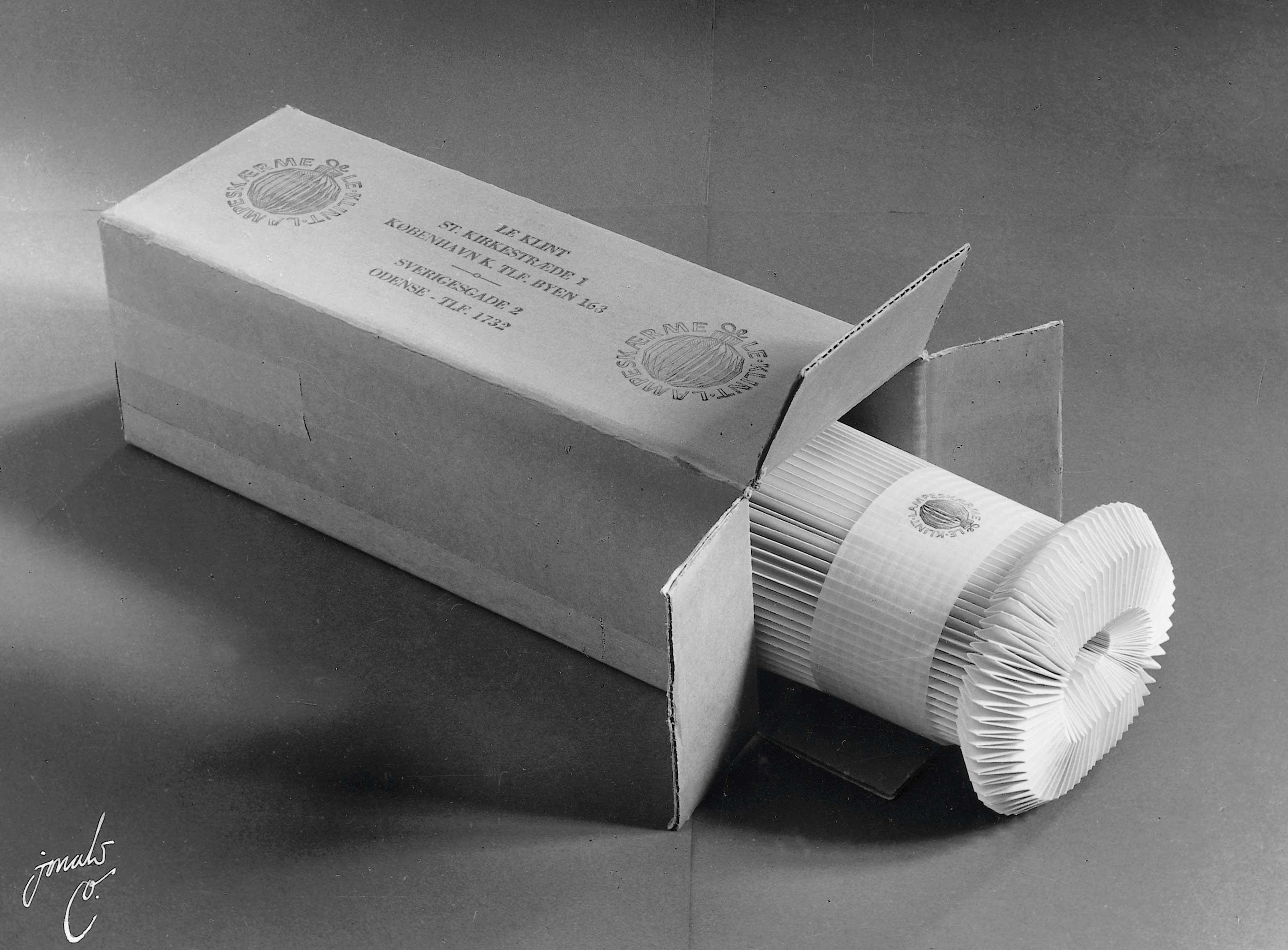 sort/hvid billede af en foldet lampeskærm liggende indpakket i emballage